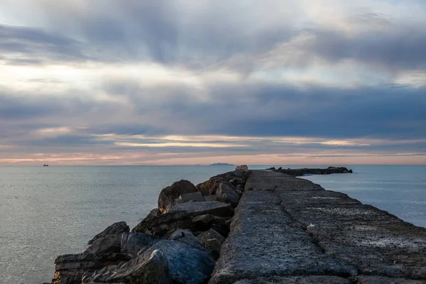 A pier on the Mediterranean Sea in Tuscany at sunset with an island in the background