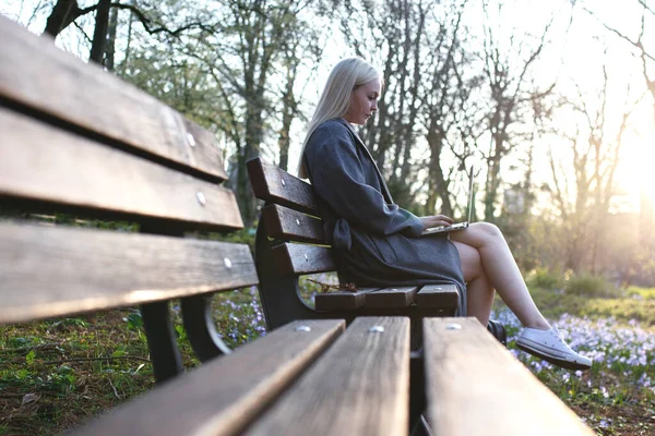 Parktaki bankta dizüstü bilgisayarıyla çalışan sarışın kız..