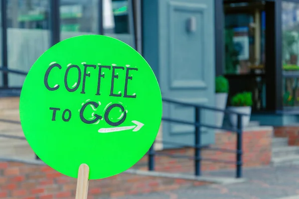 coffee to go sign is located on a green wooden advertising board on the street