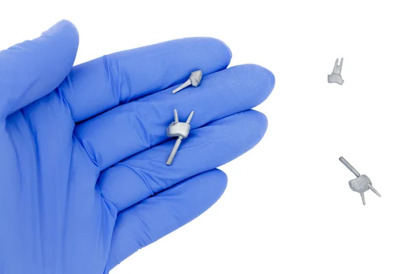 Dental pins, posts and cast posts in the dentist's hand. in a glove there is a cast pin on a white background. restoration of teeth with great deterioration 스톡 사진