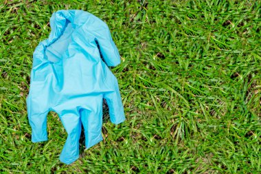 Mavi kullanılmış tıbbi eldiven yeşil çimlerin üzerinde duruyor. Bir insanı koronavirüsten koruma kavramı. Doktorların virüse karşı korunması. Uzayı kopyala Düz yatıyordu