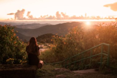 Bulanık görüntü, oturan ve gün batımını izlemek yalnız kadın 