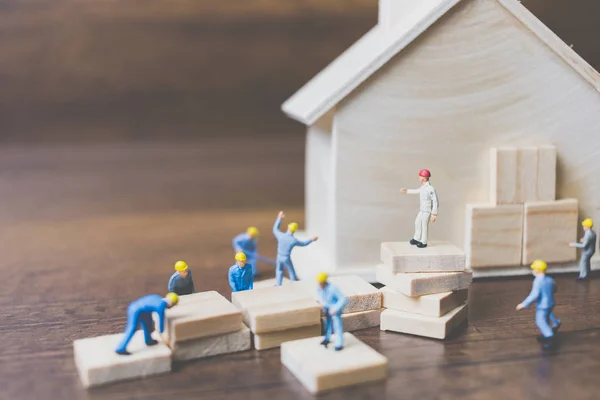 Miniature workers team build a wooden house