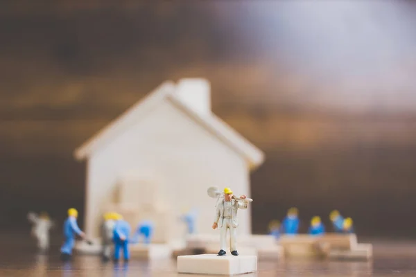 Miniature workers team build a wooden house