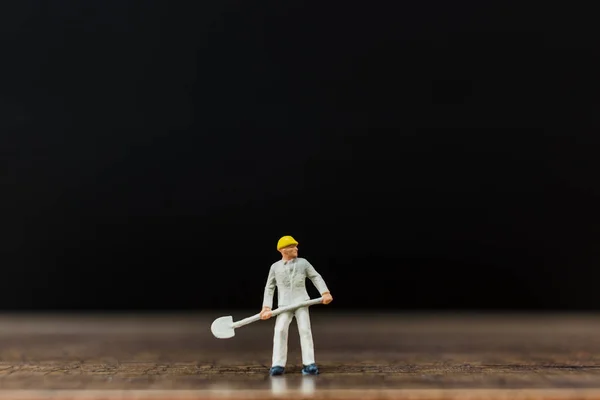 Trabajador en miniatura sobre suelo de madera con fondo negro — Foto de Stock