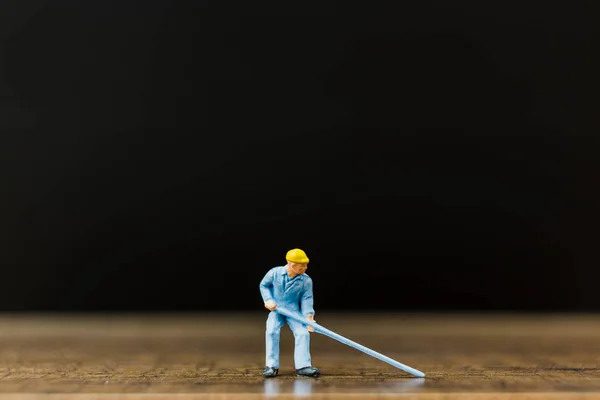 Trabajador en miniatura sobre suelo de madera con fondo negro — Foto de Stock