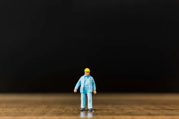 Trabajador en miniatura sobre suelo de madera con fondo negro — Foto de Stock