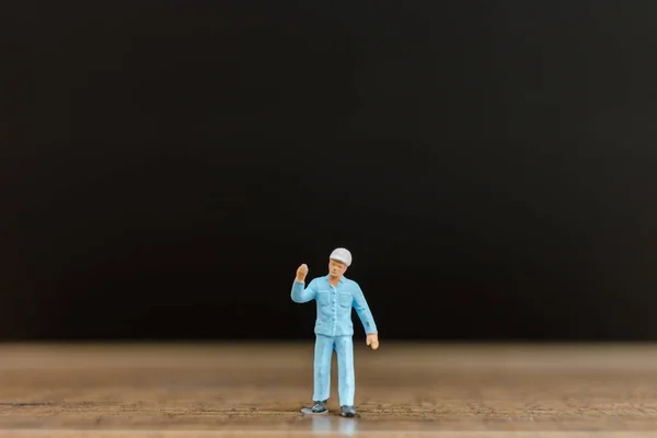 Trabajador en miniatura sobre suelo de madera con fondo negro — Foto de Stock