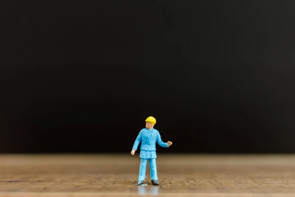 Trabajador en miniatura sobre suelo de madera con fondo negro — Foto de Stock