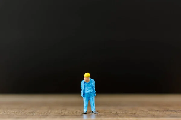 Miniatuur mensen werknemer op houten vloer met zwarte achtergrond — Stockfoto
