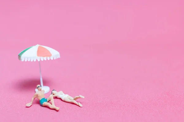 Miniaturmenschen im Badeanzug entspannen auf rosa Hintergrund — Stockfoto