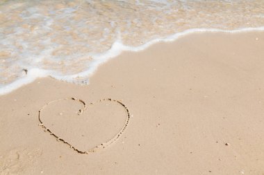 Sahilde bir kalp ve arka planda dalgalar.