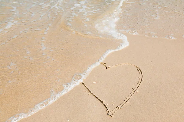 Herz auf Sand am Strand mit Welle im Hintergrund — Stockfoto