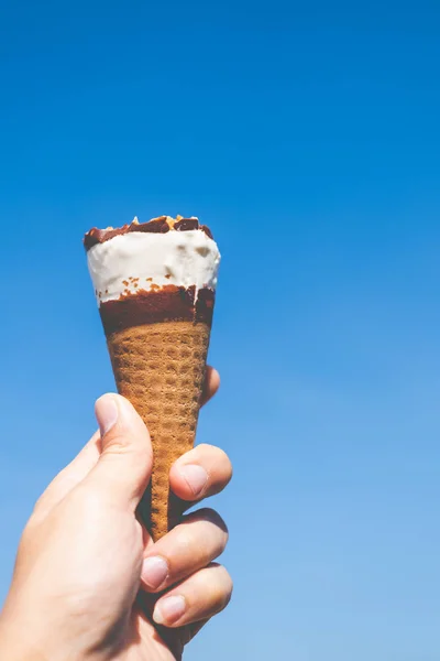 Mão segurando um cone de sorvete com fundo azul céu — Fotografia de Stock