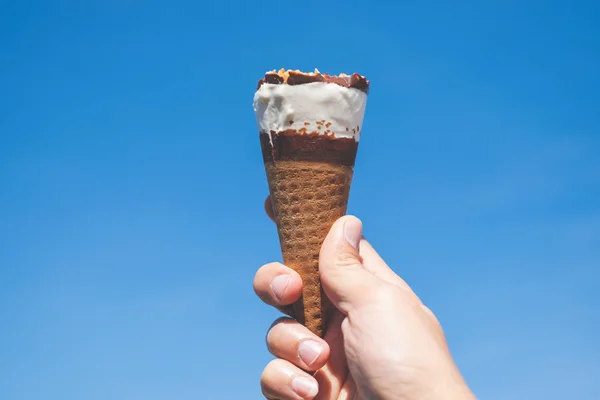 Mão segurando um cone de sorvete com fundo azul céu — Fotografia de Stock