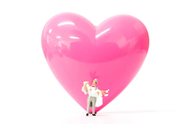 Coppia di persone in miniatura con cuore rosa su sfondo bianco, concetto di San Valentino — Foto Stock