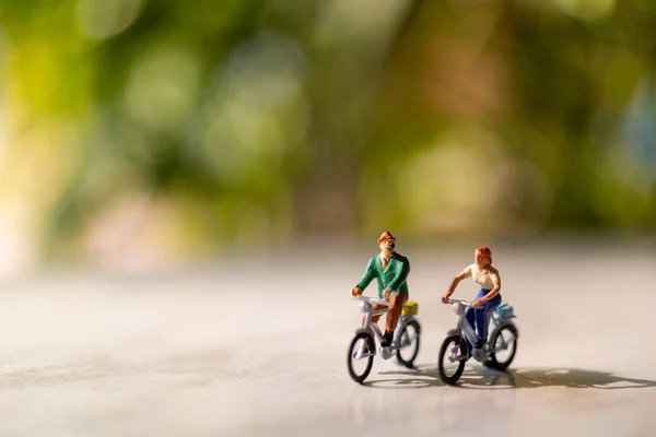 Miniaturmenschen fahren Fahrrad im Freien mit grünem Bokeh-Hintergrund — Stockfoto