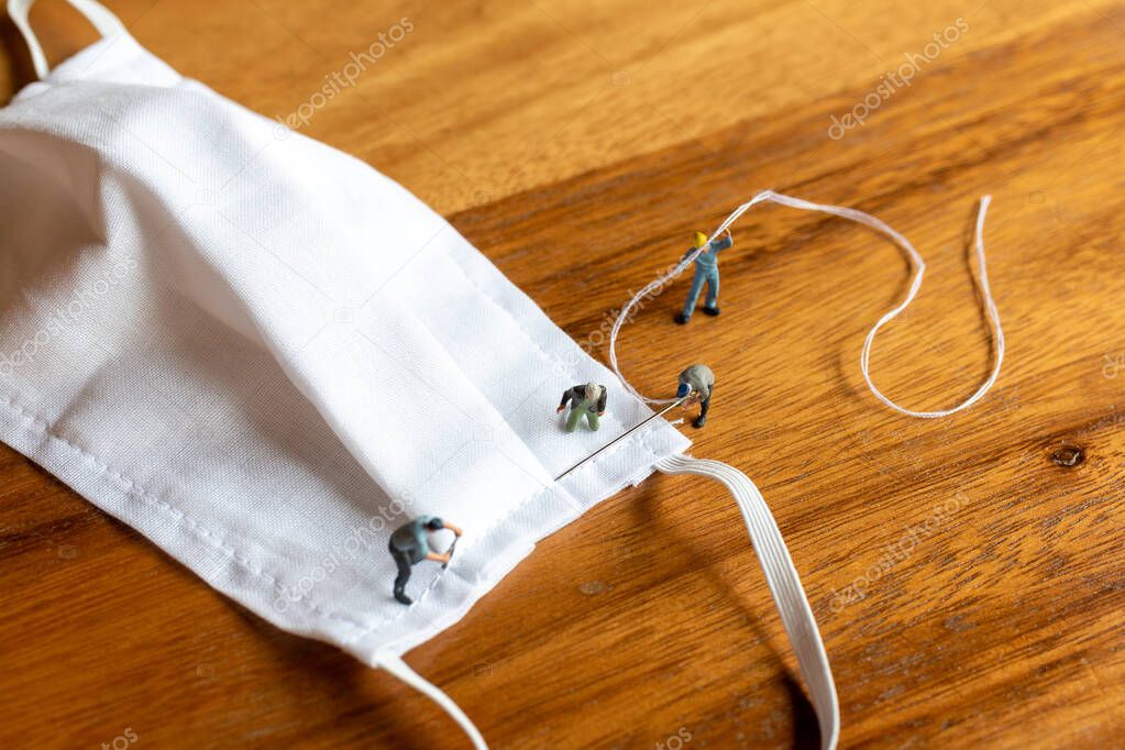 Miniature people : worker team making a homemade mask from white fabric on wood table backgroud