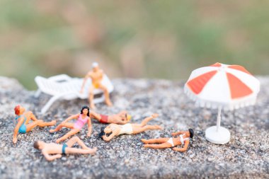 Minyatür insanlar mayo giyip bir kayanın üzerinde güneşleniyorlar.