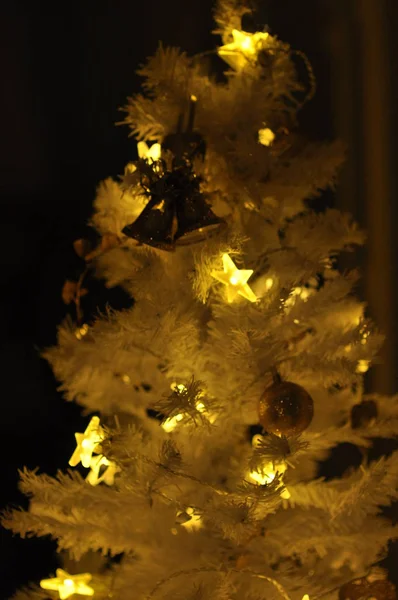 Plastic white Christmas tree indoors with decoration and lights on, on a black background — Stock Photo, Image