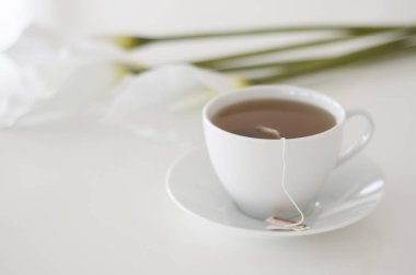 Çay saati geldi! İngiliz ikindi çayı, beyaz çay fincanı ve arka planda beyaz arum çiçekleri.
