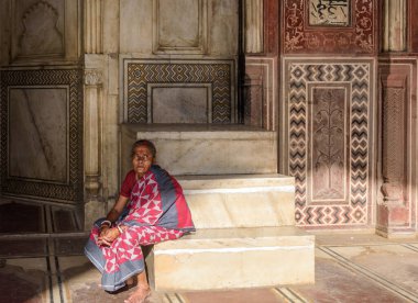 Agra, Uttar Pradesh / Hindistan - 21 Mart 2019: Bir kadın, Tac Mahal 'e bakan kırmızı kumtaşı camiinin içindeki kürsünün yanındaki merdivenlerde oturuyor. Arka plandaki duvarlarda geometrik desenler var..
