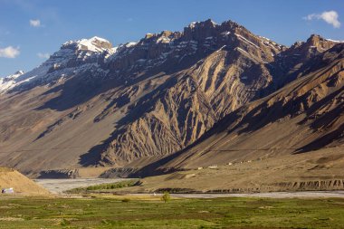 Hindistan 'ın Himachal Pradesh kentindeki Spiti nehri ve yeşil tarlalar üzerinde yükselen dik, yüksek, kayalık dağlar..