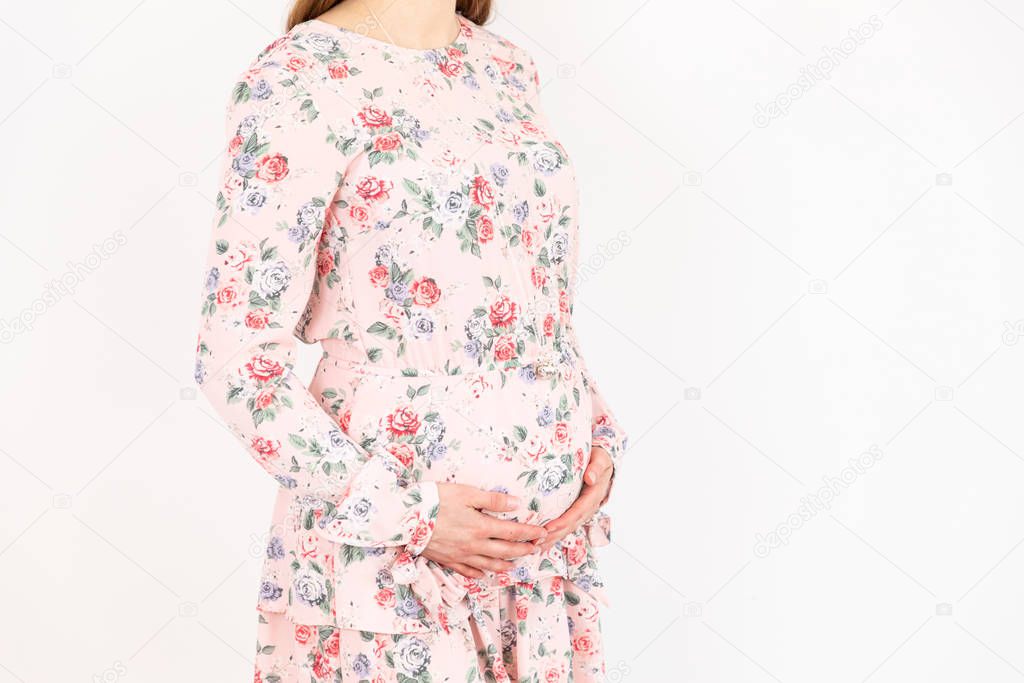Young pregnant woman with pink dress puts her hands on her belly