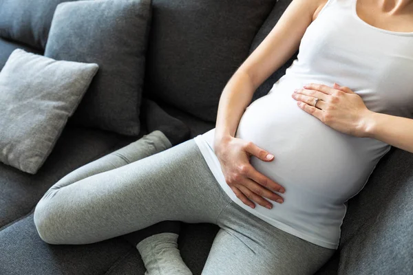 Mladá těhotná žena drží své břicho sedí na pohovce — Stock fotografie