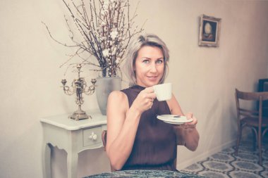 Pencerenin yanındaki kafede ya da restoranda oturan ve kahve içen güzel sarışının ön görüntüsü.