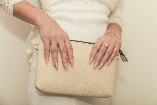A noiva em um vestido de casamento mantém na mão uma bolsa branca. Bela manicura. Dia do casamento. Anéis de casamento . — Fotografia de Stock