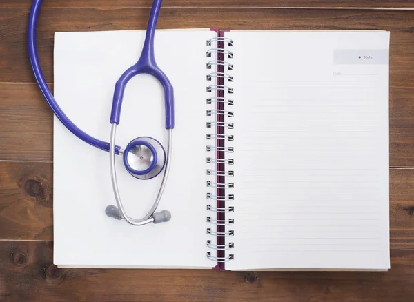Stethoskop und leeres Notizbuch auf Holztisch — Stockfoto