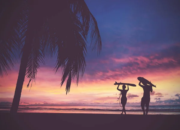 Silueta De personas surfistas que llevan su tabla de surf en la puesta del sol b — Foto de Stock