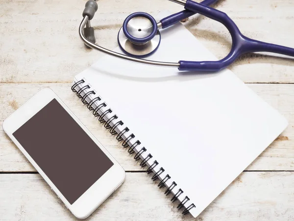 Smartphone with stethoscope and notebook on wooden background — Stock Photo, Image