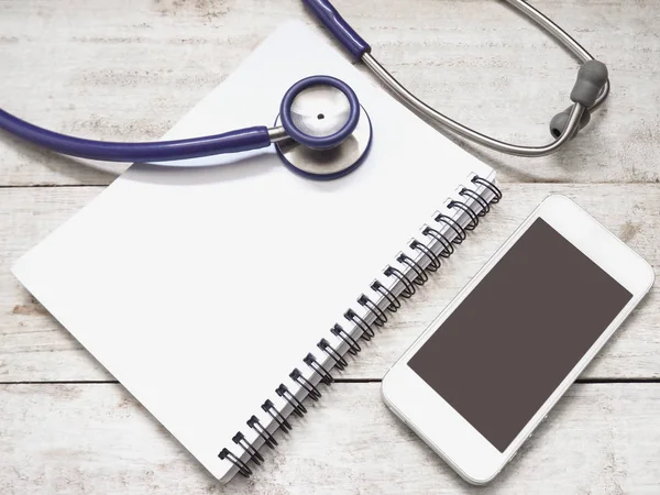 Smartphone mit Stethoskop und Notizbuch auf Holzgrund — Stockfoto