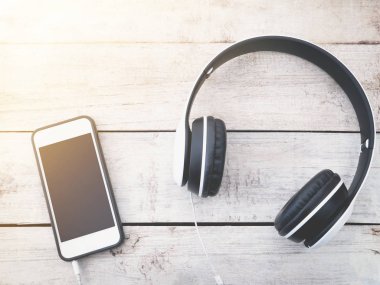 Kulaklık ve Beyaz ahşap arka plan üstünde hareket eden telefon. 