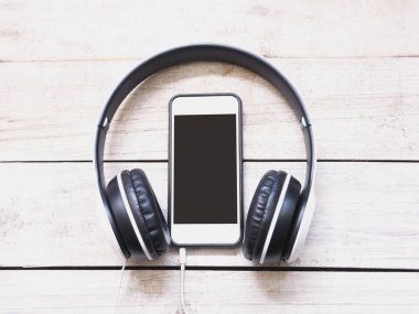 Kulaklık ve Beyaz ahşap arka plan üstünde hareket eden telefon.