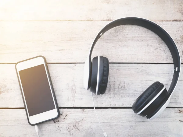 Kulaklık ve Beyaz ahşap arka plan üstünde hareket eden telefon. 