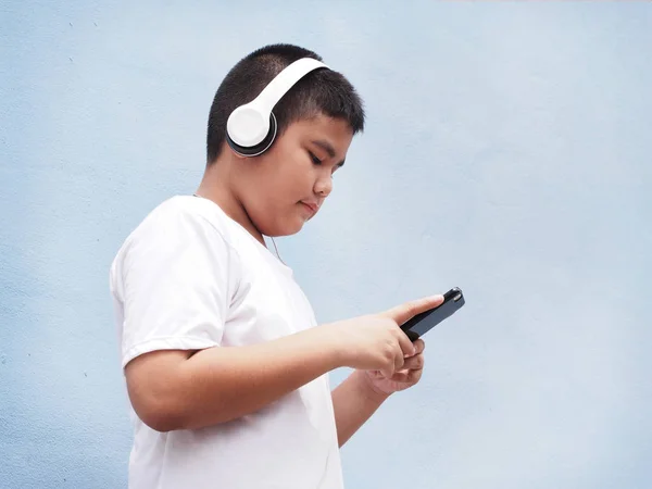 Azjatycki chłopiec z białą koszulę, noszenie słuchawek i gry mobilne — Zdjęcie stockowe