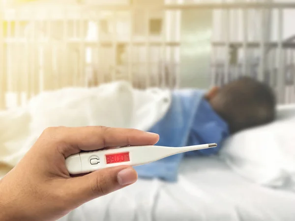 Hand digitale thermometer met hoge koorts hebt over wazig ziekte Aziatische jongen — Stockfoto
