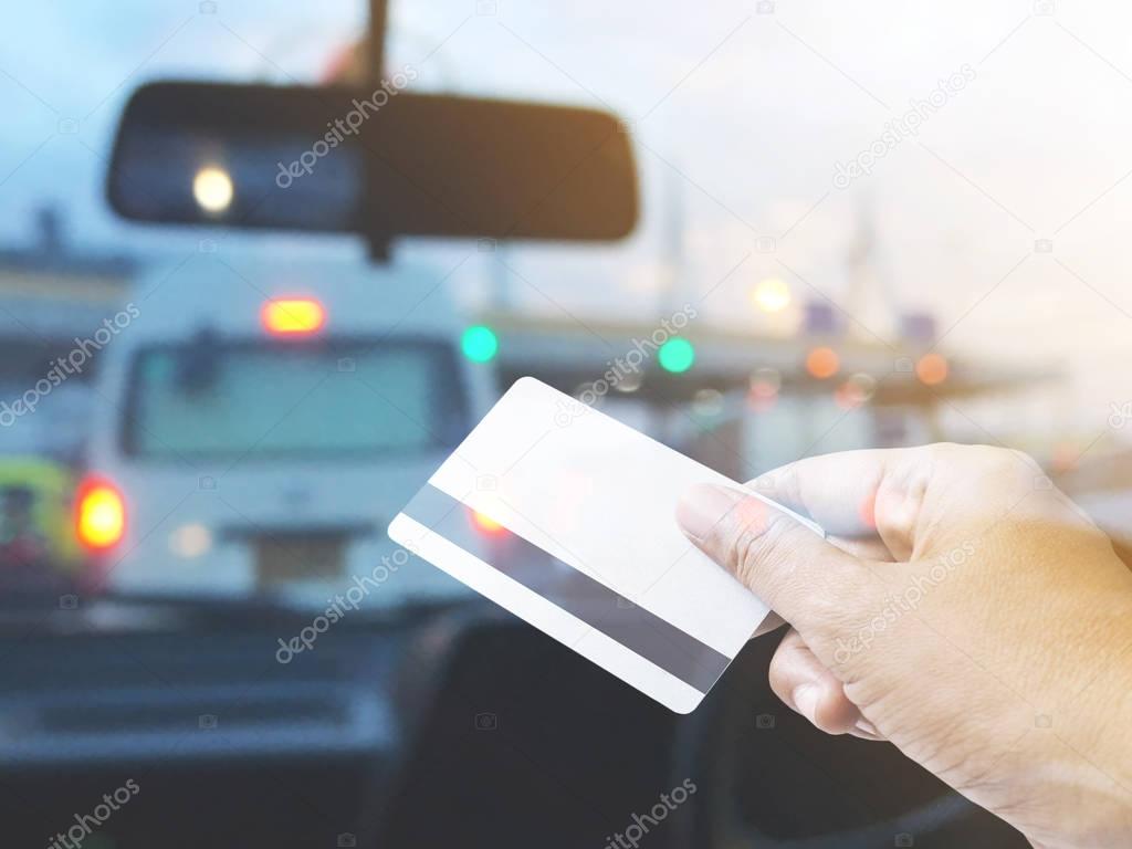 Hand holding credit card over blurred background of car at pay toll station