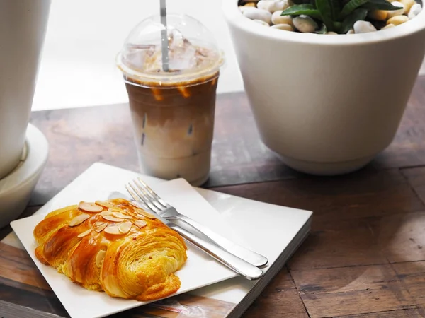 面包杏仁在白色盘子和玻璃冰拿铁咖啡 — 图库照片