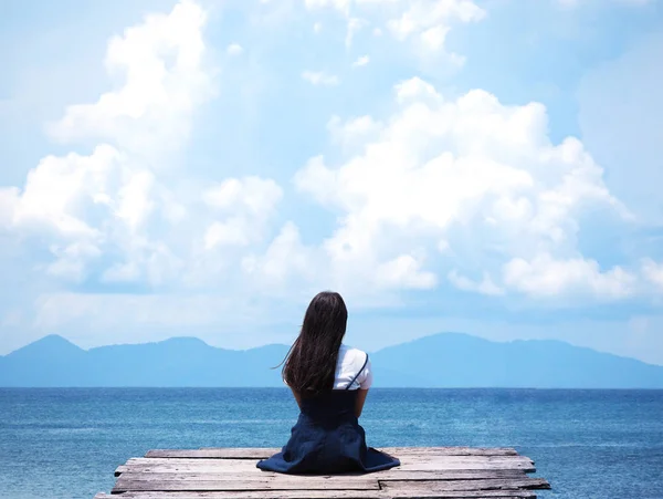 Asiático chica sentado en madera puente sobre azul mar fondo — Foto de Stock