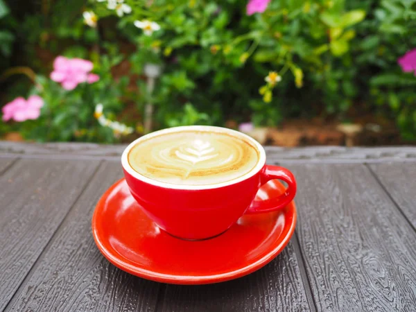 花园里木制桌子上的红杯拿铁咖啡. — 图库照片