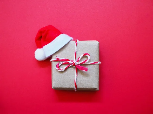 Cerrar caja de regalo hecha a mano y sombrero de Santa Claus sobre fondo rojo —  Fotos de Stock