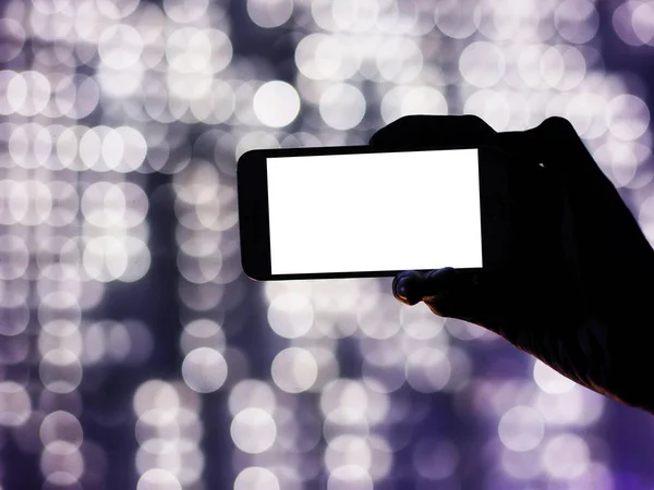 Силуэт руки, держащей мобильный телефон с пустым белым экраном — стоковое фото