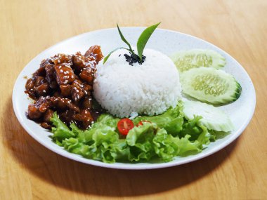 Beyaz pirinci, tatlı domuz eti ve sebzelerle kaplayın. Tahta masanın üzerinde beyaz tabakta..