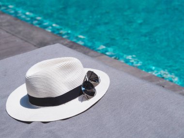 Yüzme havuzunun yanındaki sandalyeye beyaz hasır şapka ve güneş gözlüğü tak. Yaz tatili konseptine tatil.