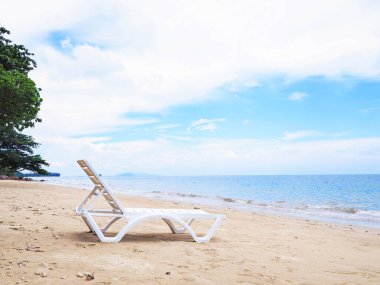 Kumlu sahilde beyaz güneş yatağı mavi gökyüzüne karşı. Mutlu yaz tatilleri..