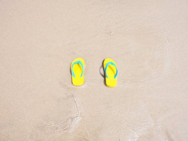 Bej rengi kum yaz plajı arka planında sarı sandaletin en üst görüntüsü. Tatil tatili kavramı.